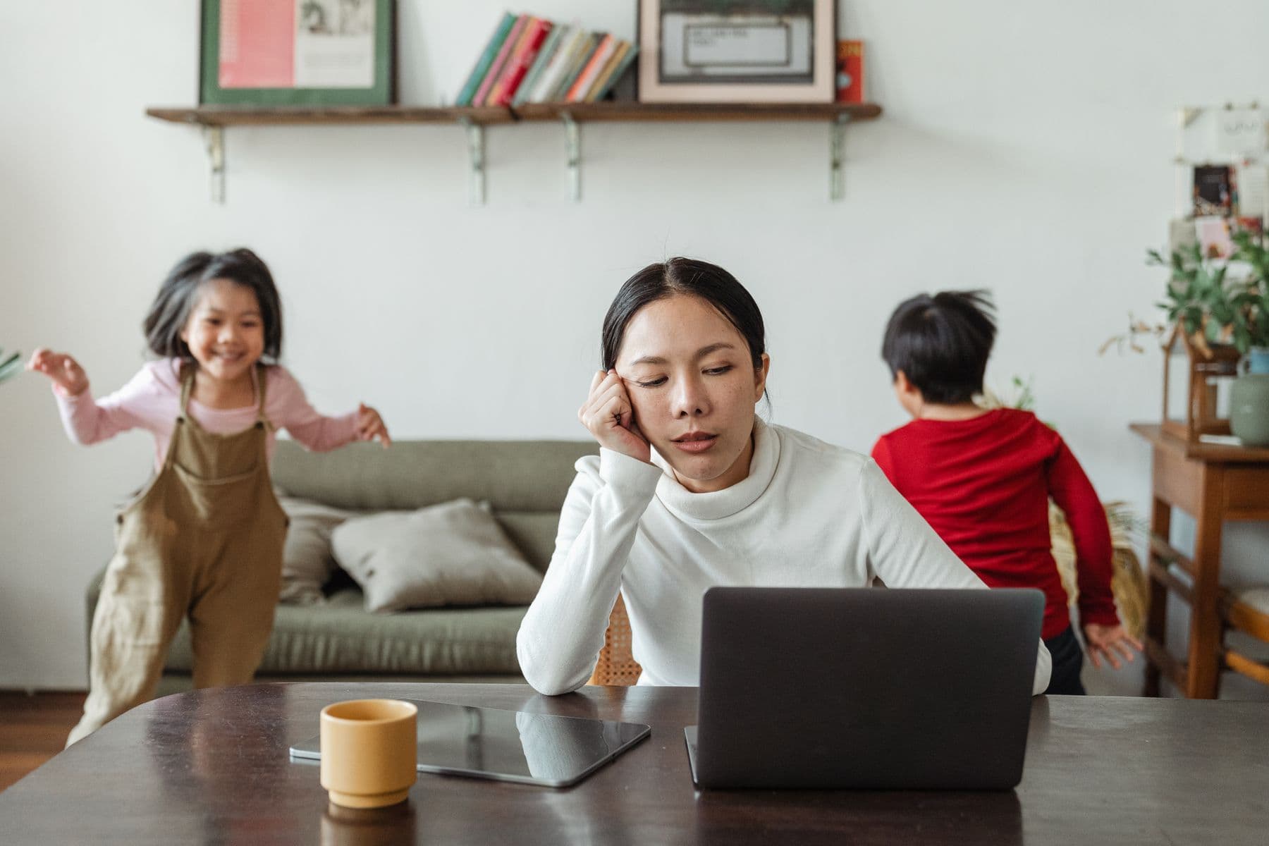 A mother working at her laptop while her children play nearby